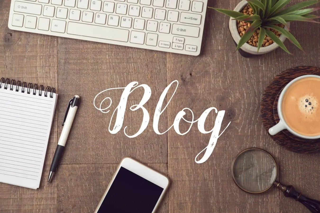 Íróasztal jegyzettömbbel, laptoppal, okostelefonnal, nagyítóval és kávéval.