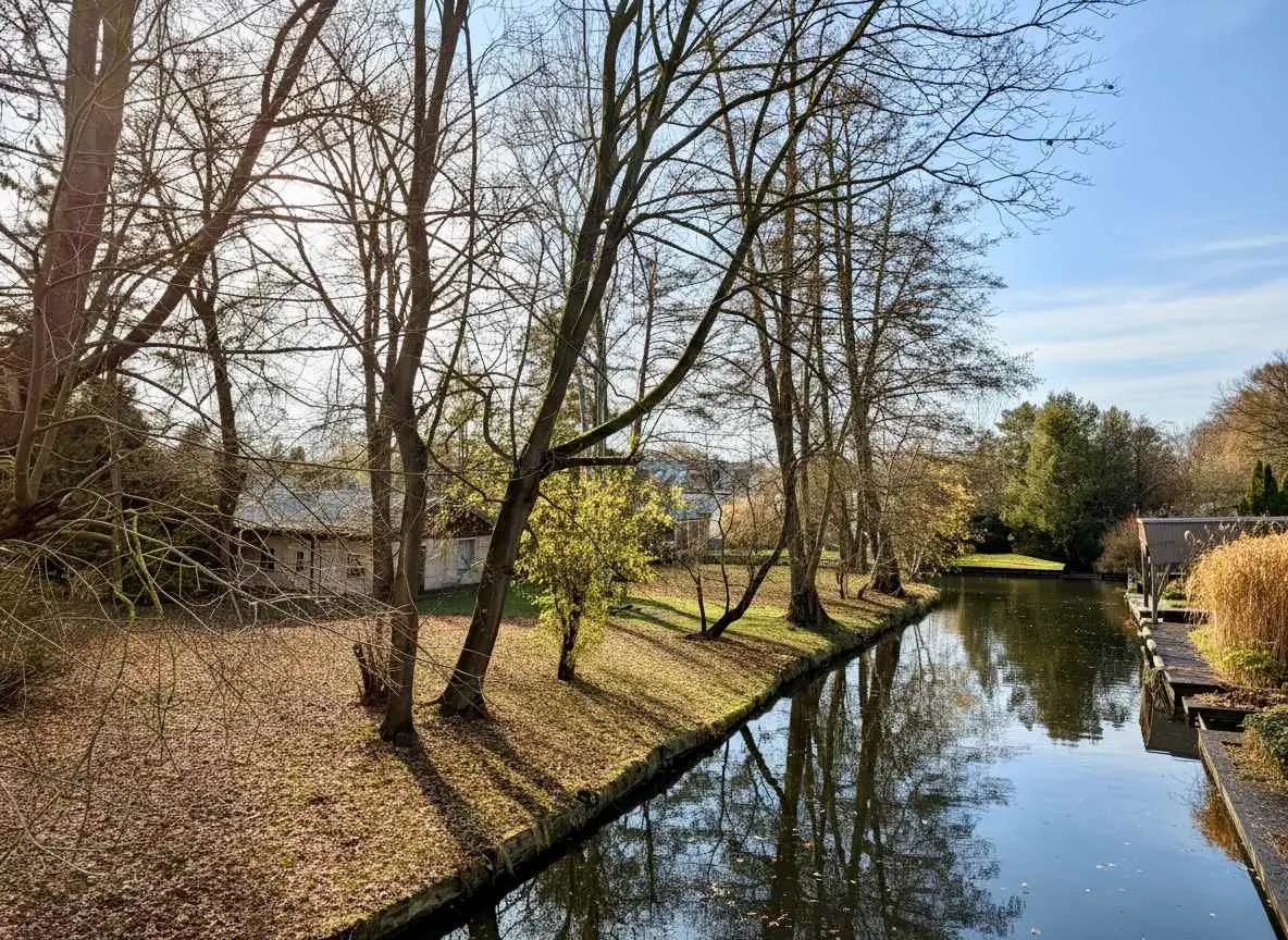 Wassergrundstück in Neu-Venedig (Berlin) mit ruhigem Kanal, Uferböschung, Baumbestand und sonniger Gartenfläche am Wasser.